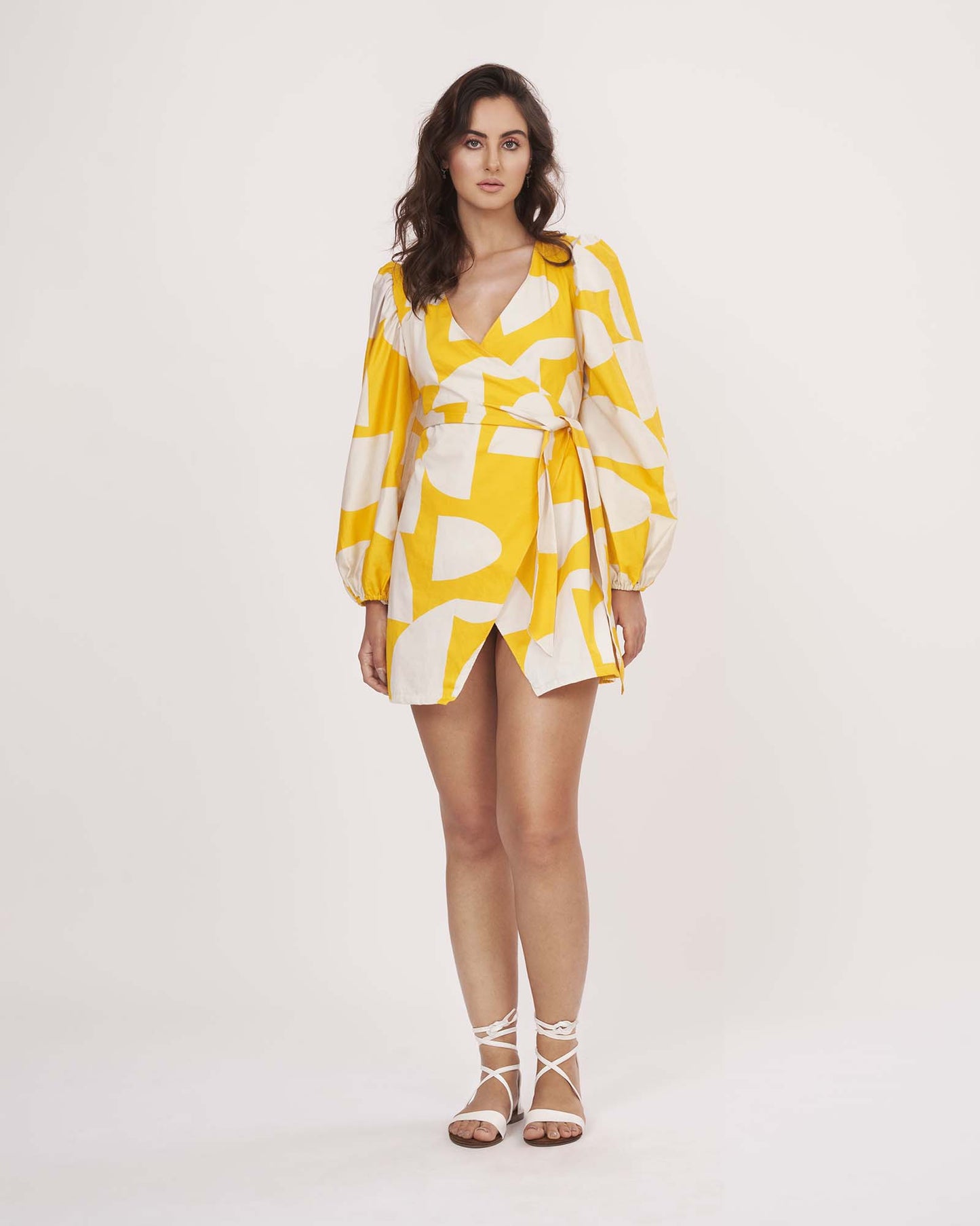 Walking pose of model in yellow printed wrap dress, showcasing movement and fit.