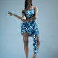 Angled pose of model in blue abstract dress, one hand raised slightly, showing side slit and fit.