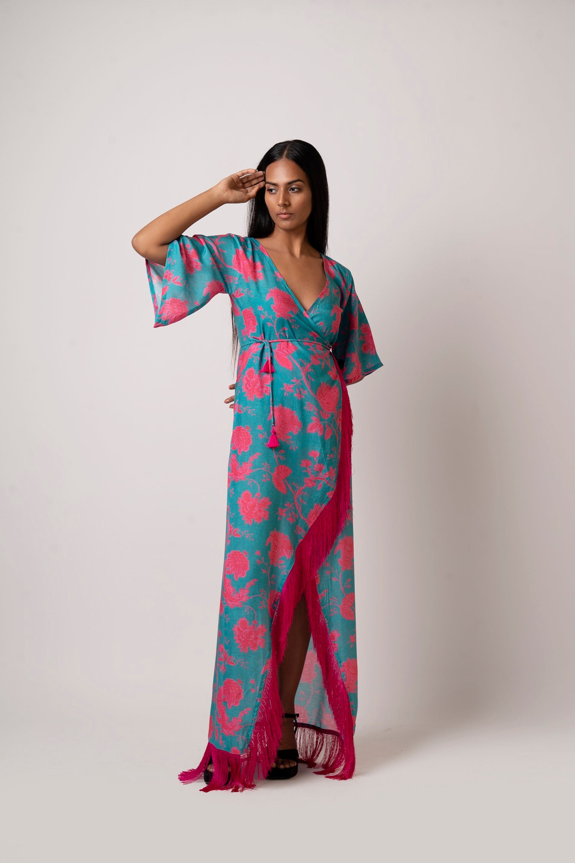 Close-up side angle of model in floral blue and pink wrap dress, highlighting neckline, sleeve, and waist tassels.