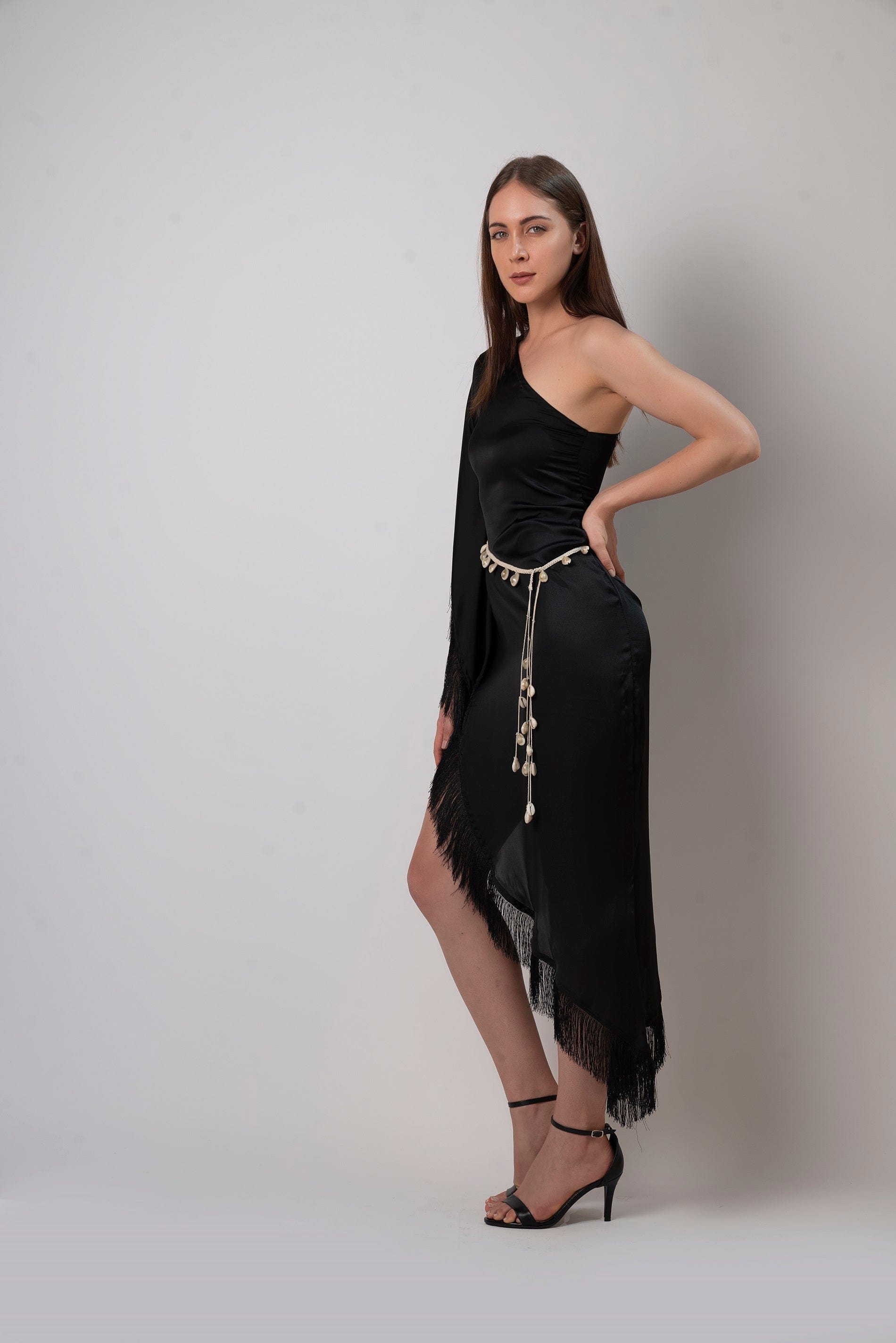 Side-angle studio view of model in black asymmetric kaftan dress showing hemline and silhouette.