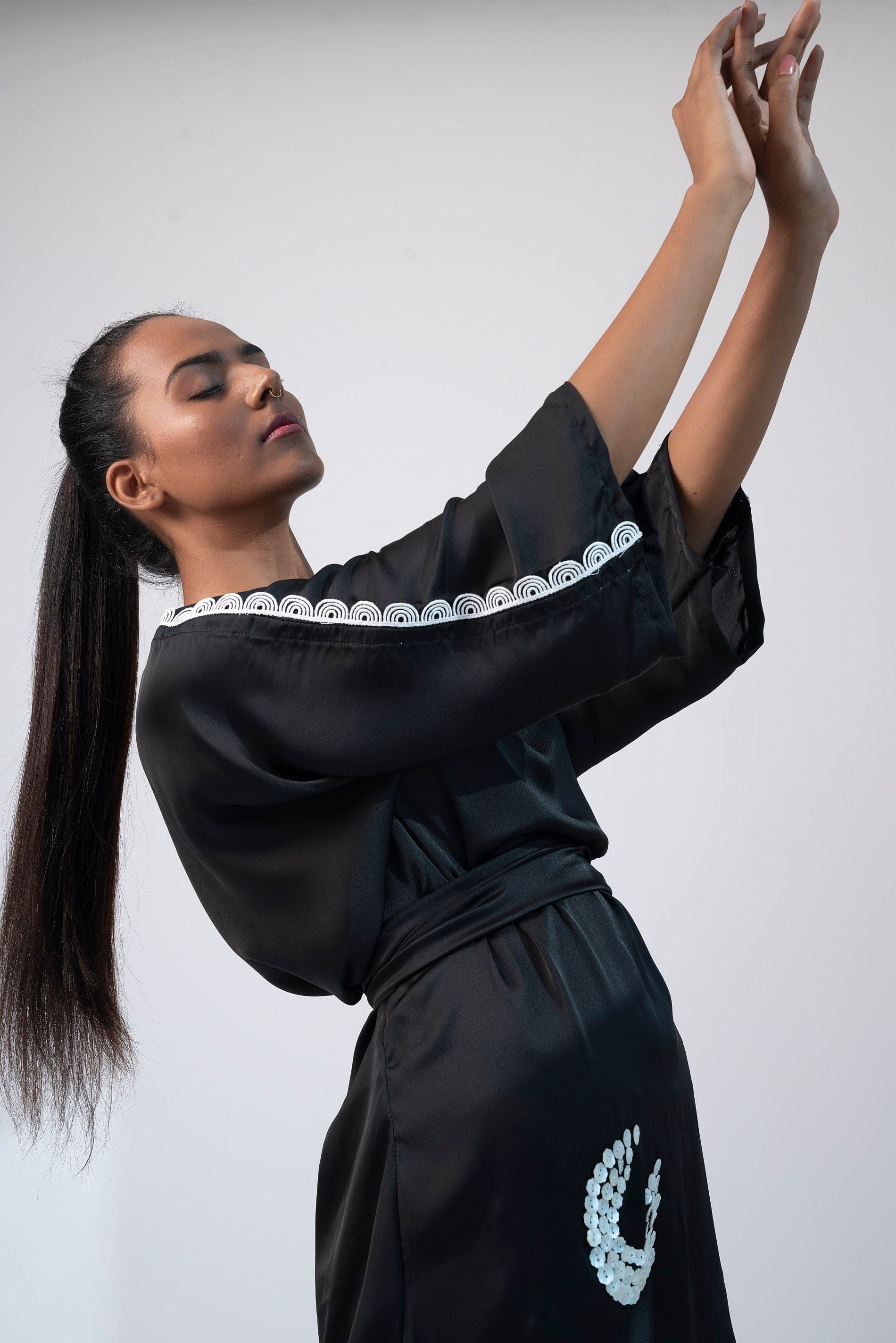 Side view of black kimono mini dress with one hand raised and lace hem visible.