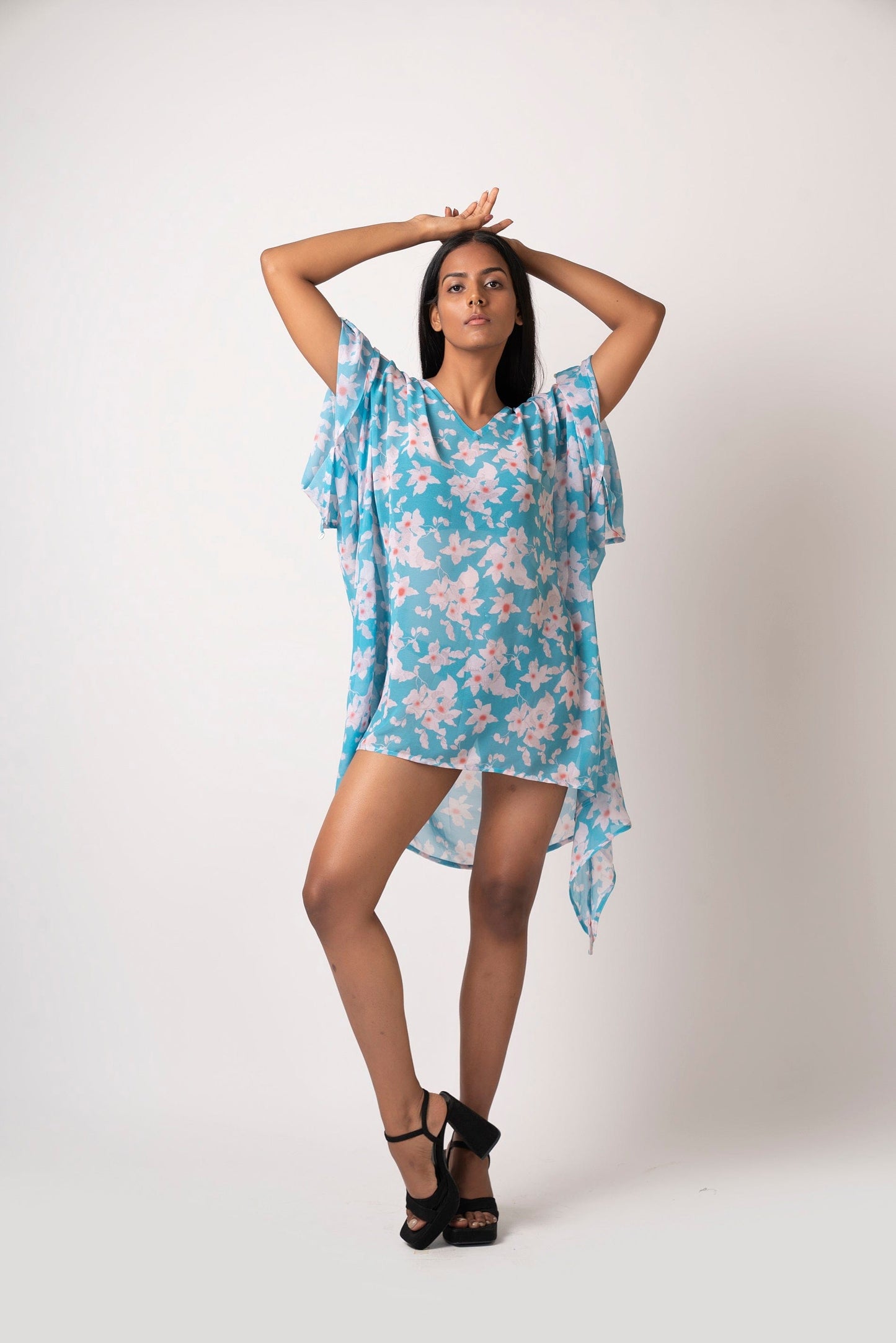 Blue floral georgette dress in kimono style, model with hands raised above head in playful pose.