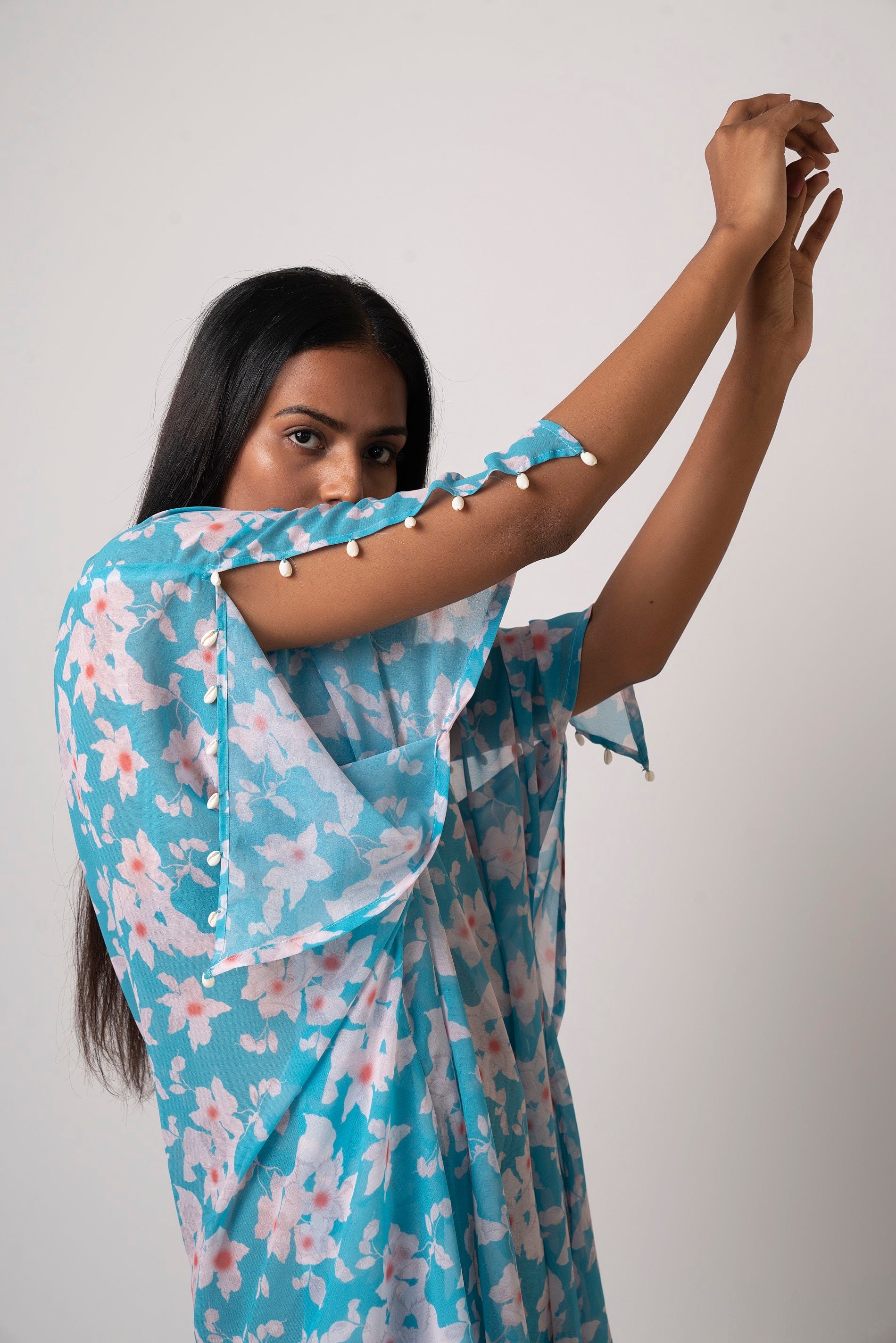 Close-up of model lifting arm in blue georgette dress showing slit sleeve and seashell detailing.