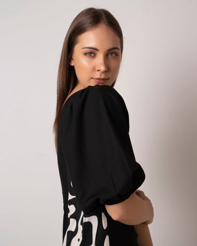 Close side angle of one-shoulder black mini dress highlighting shell-embellished side panel.