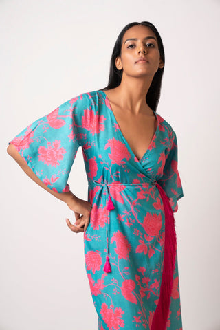 Front-facing pose of model in floral blue muslin dress with side tie-up and flared hem, holding one hand at the waist.