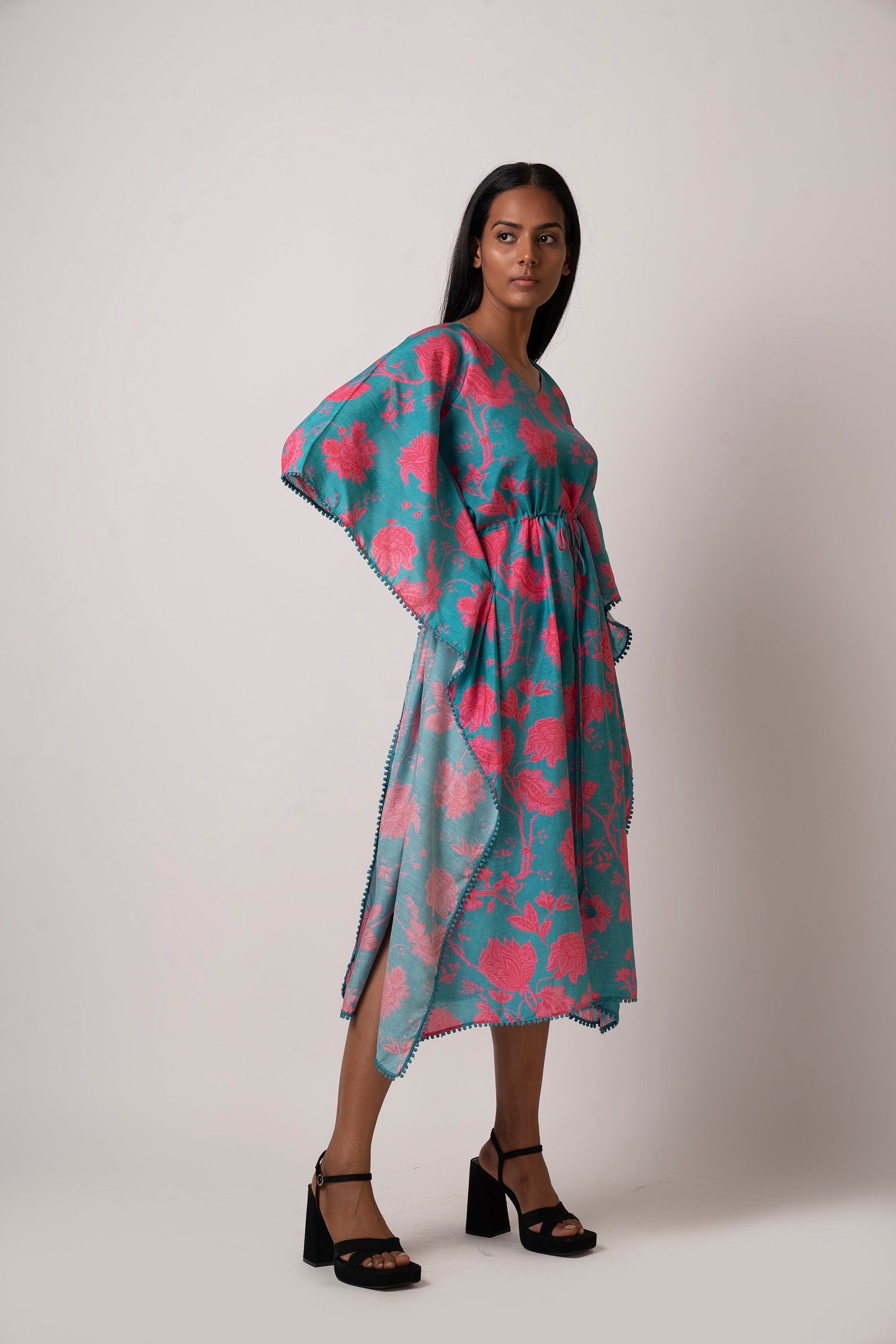 Angled standing pose of model in blue and pink floral printed kaftan dress with one leg slightly forward.