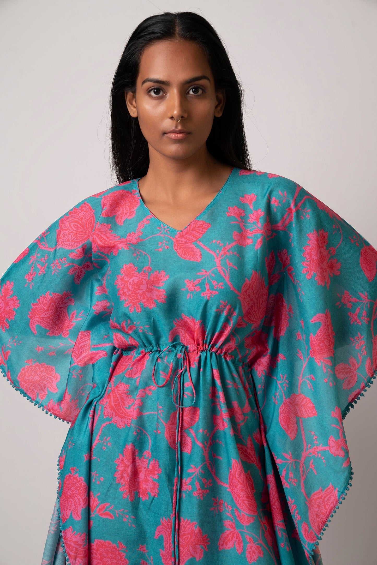 Close-up front view of model in floral printed muslin kaftan with V-neck and wide sleeves, looking straight ahead.
