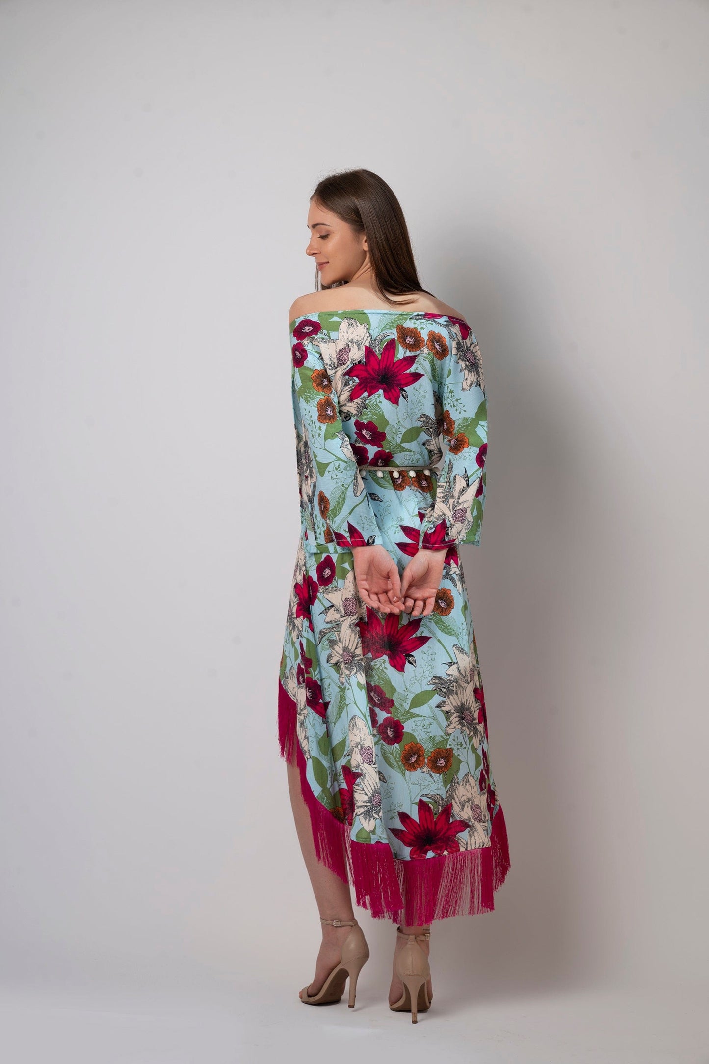 Rear-angle view showing back fit of the off-shoulder blue printed beach dress with relaxed silhouette and fringe hem.