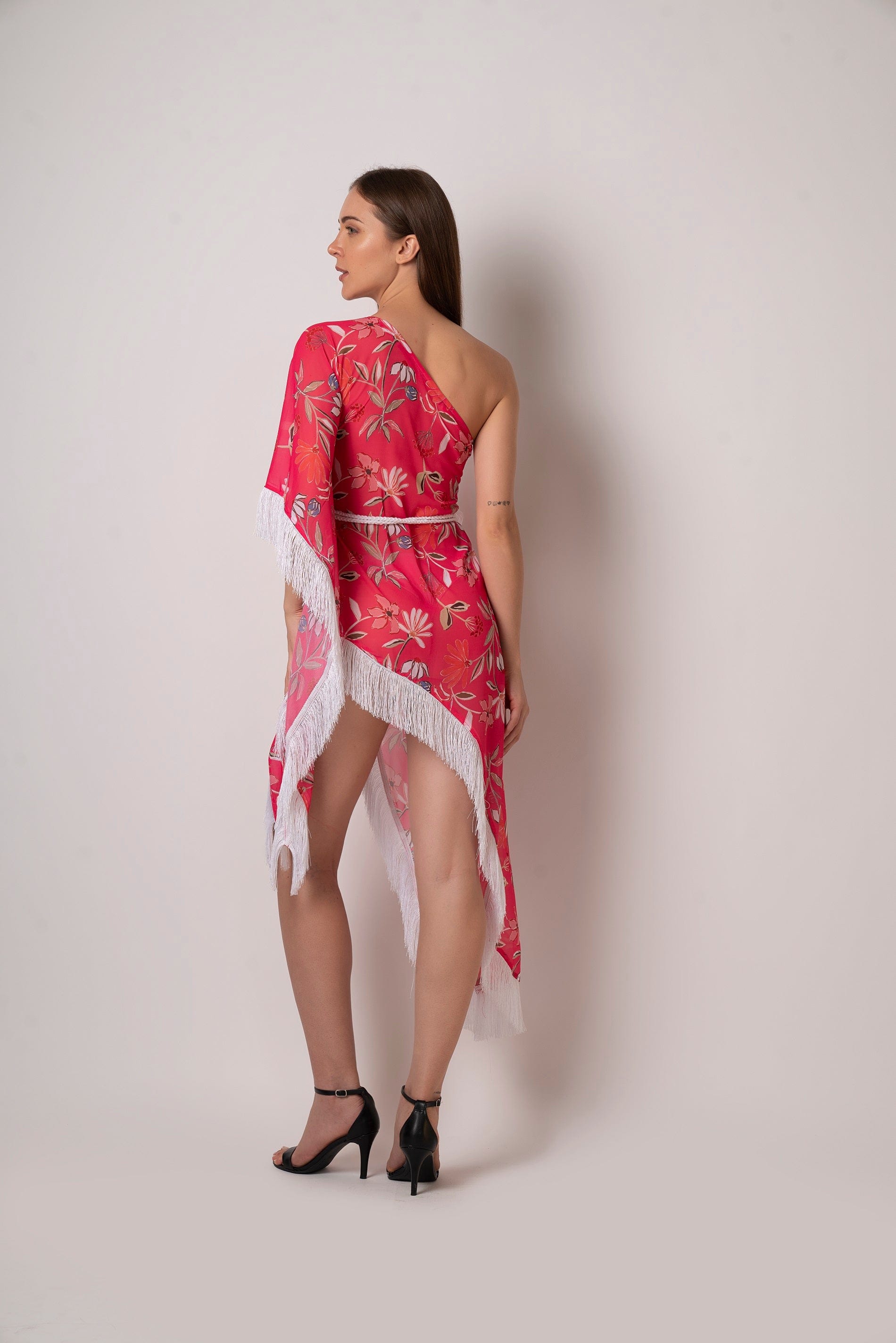 Rear view of the kaftan-style dress showing the asymmetric hem, one-shoulder silhouette, and back fall of the belt.