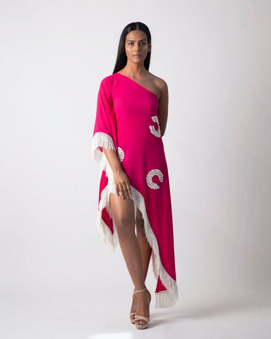 Model poses with one leg raised and slightly bent, showcasing the asymmetrical hem and fringe details of the pink one-shoulder georgette kaftan dress