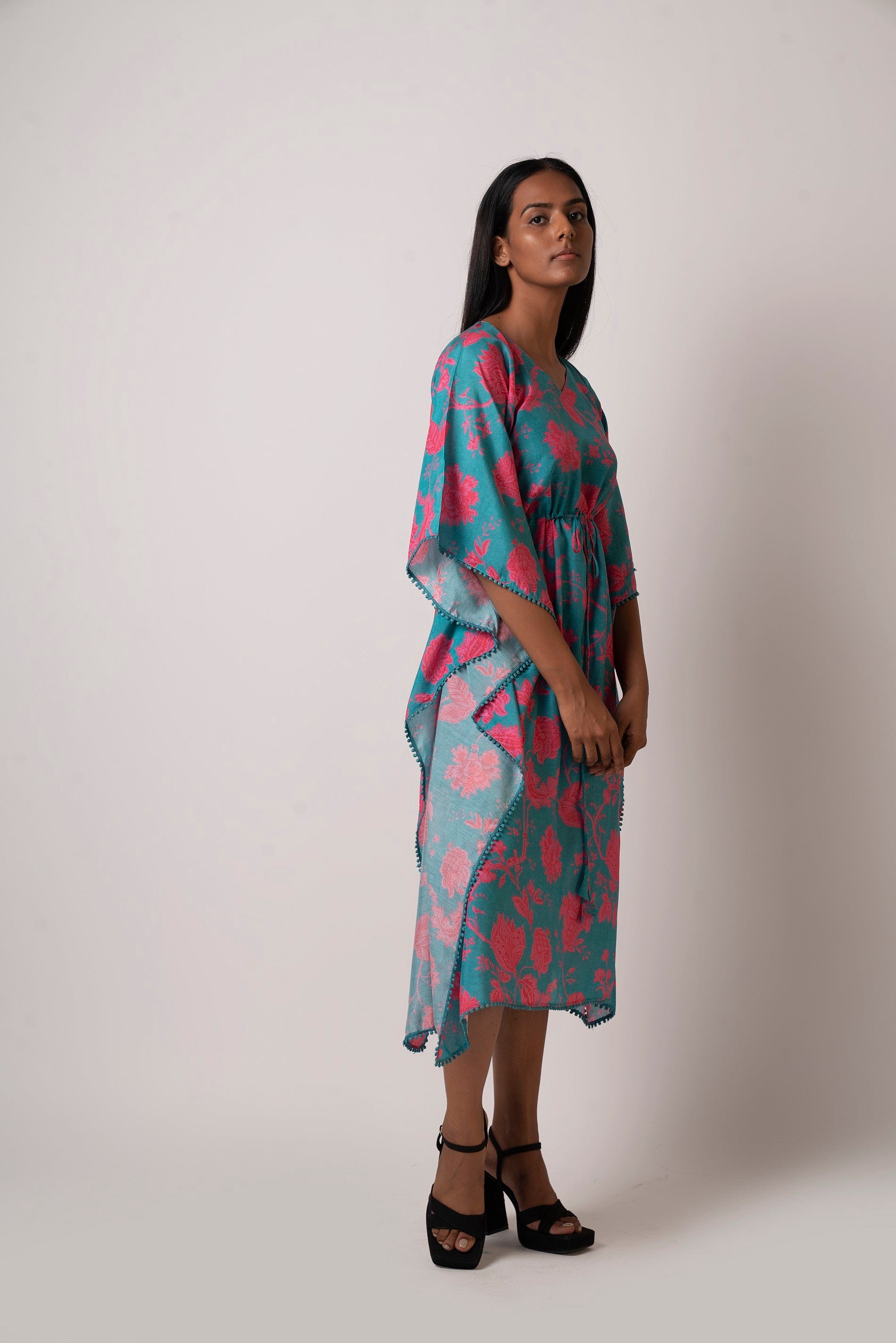 Side walking pose of model in blue floral kaftan dress with tie-up waist and 3/4 length sleeves.