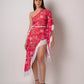 Walking pose of model in asymmetrical pink printed dress with one-shoulder design and flowing fringe hem.