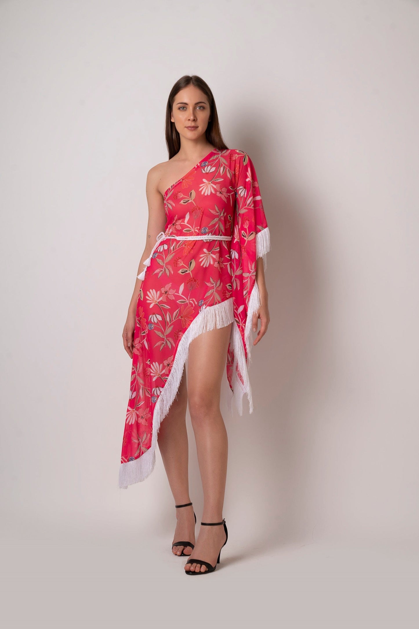Walking pose of model in asymmetrical pink printed dress with one-shoulder design and flowing fringe hem.