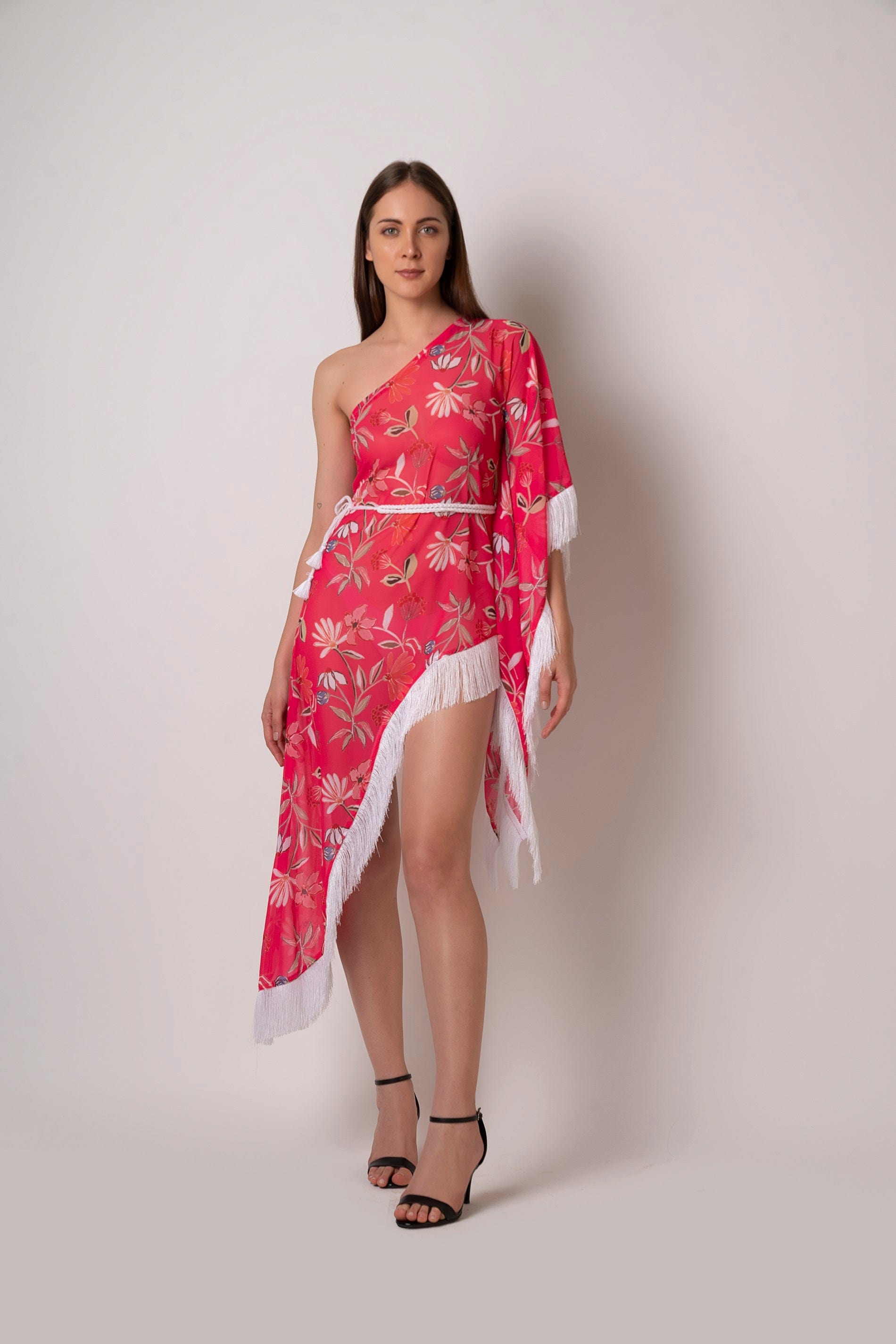 Walking pose of model in asymmetrical pink printed dress with one-shoulder design and flowing fringe hem.