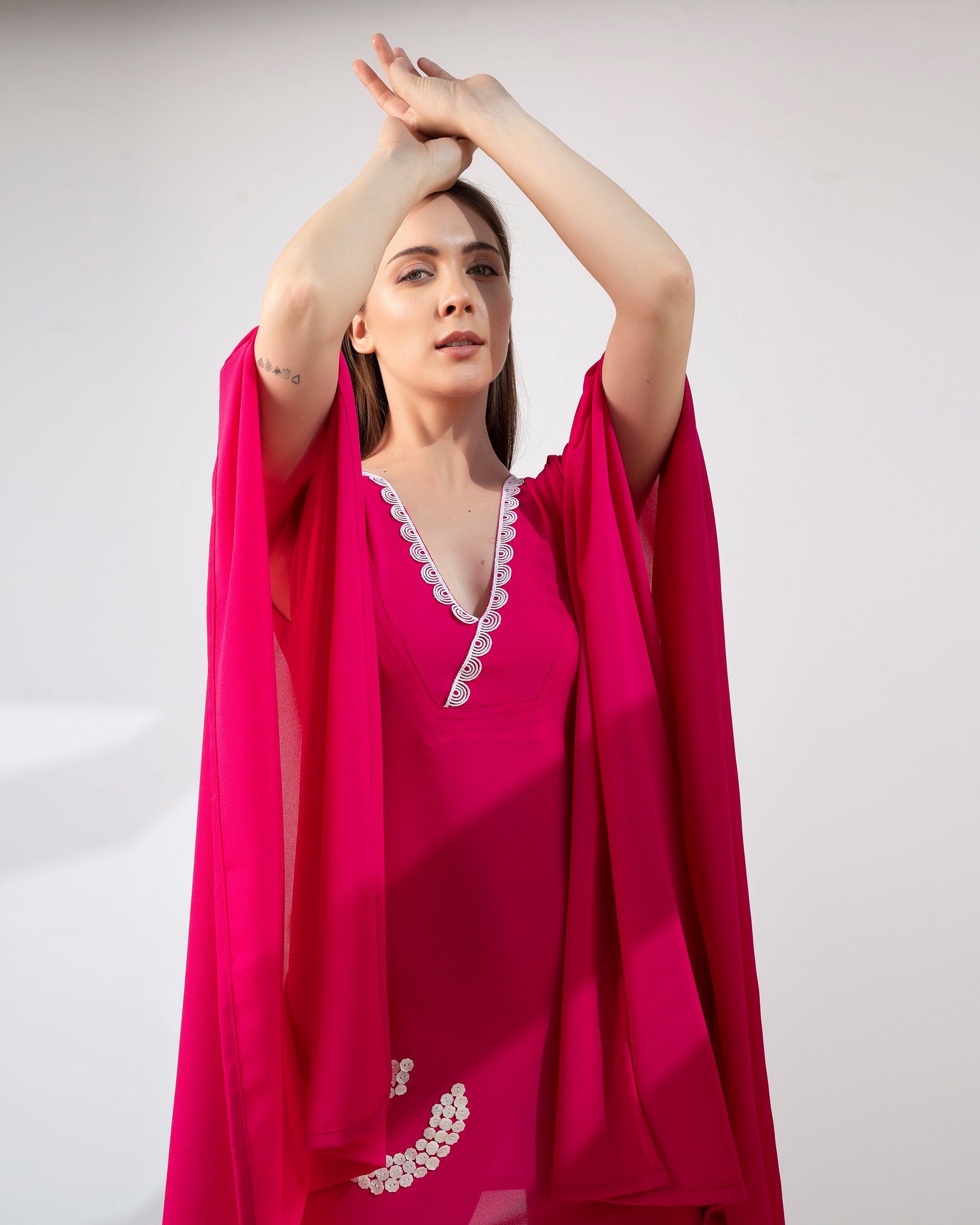 Close-up of pink kaftan dress with shell embroidery, lace detailing, and relaxed v-neckline.