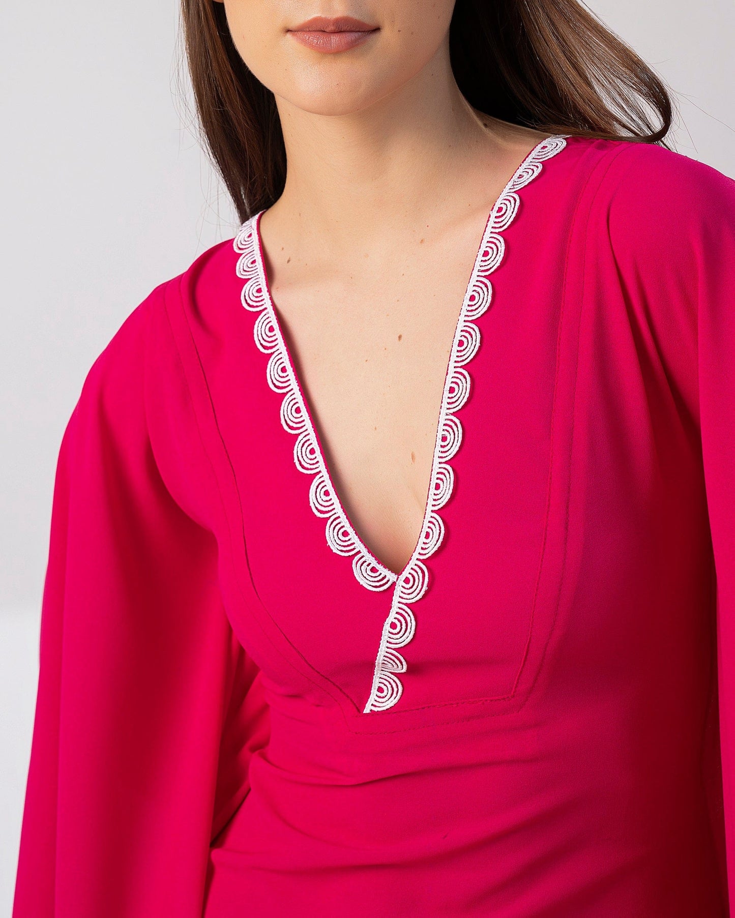 Close-up view of lace-embellished neckline and relaxed v-cut on pink kaftan dress.