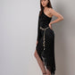 Side-angle studio view of model in black asymmetric kaftan dress showing hemline and silhouette.