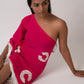 Model seated in a relaxed pose in the pink embroidered georgette dress, accentuating the flowy fabric, one-shoulder cut, and breezy beachwear feel.