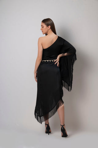 Rear view of black one-shoulder kaftan dress showcasing back drape, fringe hem, and tie-up sea shell belt.