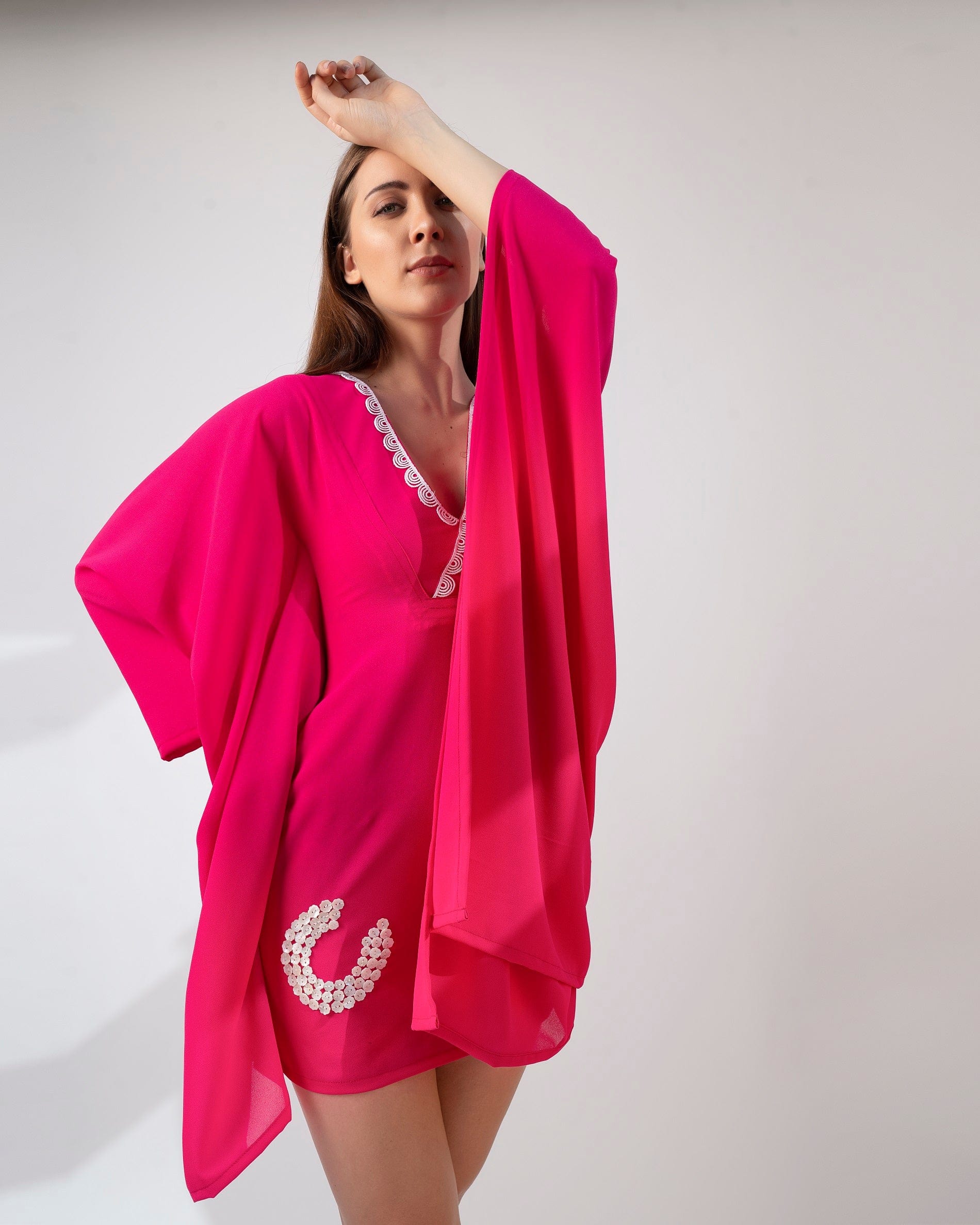 Pink kaftan dress in playful pose with one hand on head and other raised, showcasing flowy fit.
